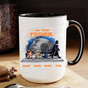 May include: White ceramic mug with a black handle and rim, featuring a Star Wars theme. The design includes the text "I AM THEIR FATHER" and illustrations of characters like Darth Vader and Baby Yoda. The mug is approximately 4 inches tall.