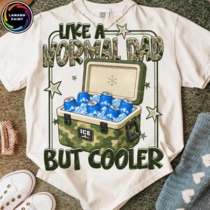 K&ouml;nnte beinhalten: Wei&szlig;es T-Shirt mit einem Grafikdesign, das einen Camouflage-K&uuml;hler mit Eis und blauen Dosen zeigt. Der Text lautet "LIKE A NORMAL DAD BUT COOLER" in gr&uuml;nen und braunen Buchstaben. Das Shirt hat einen Rundhalsausschnitt und kurze &Auml;rmel.