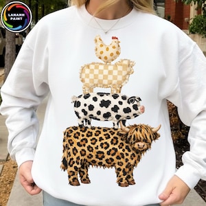 May include: White sweatshirt featuring a stack of farm animals: a Highland cow with a leopard print, a pig with black spots, a sheep with a checkered pattern, and a chicken with polka dots. The sweatshirt has the text "LANANH PAINT" in a circle.