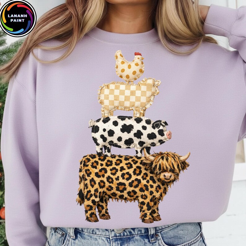 Op de afbeelding: Een lila sweatshirt met een stapel boerderijdieren. Het ontwerp omvat een kip, een schaap, een varken en een koe. De kip is gestippeld, het schaap is geblokt, het varken is gevlekt en de koe heeft een luipaardprint.