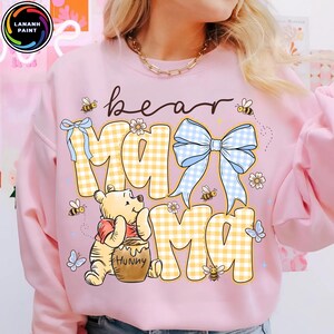 Pode incluir: Camisola rosa claro com a frase "bear mama". O design inclui um padr&atilde;o xadrez amarelo e branco, um la&ccedil;o azul, abelhas, borboletas e um urso de desenho animado com um pote de mel.