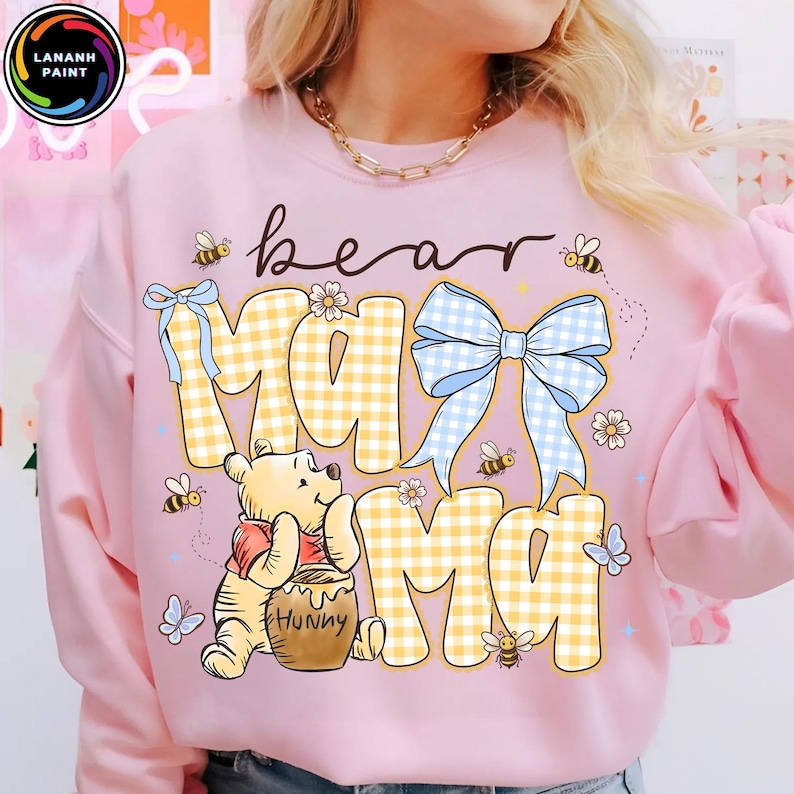 Pode incluir: Camisola rosa claro com a frase "bear mama". O design inclui um padr&atilde;o xadrez amarelo e branco, um la&ccedil;o azul, abelhas, borboletas e um urso de desenho animado com um pote de mel.