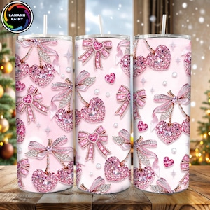 May include: Three pink tumblers with a repeating pattern of jeweled hearts, bows, and small hearts on a light pink background. Each tumbler has a white straw. The tumblers are decorated with sparkling rhinestones and a bow design.