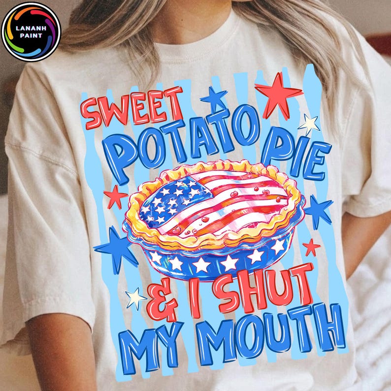 May include: Cream-colored t-shirt featuring a graphic of a sweet potato pie with an American flag design. The text reads "Sweet Potato Pie & I Shut My Mouth" in red and blue. Stars and stripes decorate the design.