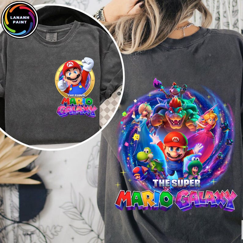 Puede incluir: Sudadera gris oscuro con un dise&ntilde;o gr&aacute;fico colorido de Mario y otros personajes del juego Super Mario Galaxy. El dise&ntilde;o incluye el texto "THE SUPER MARIO GALAXY" en una fuente multicolor. La sudadera tiene cuello redondo y mangas largas.