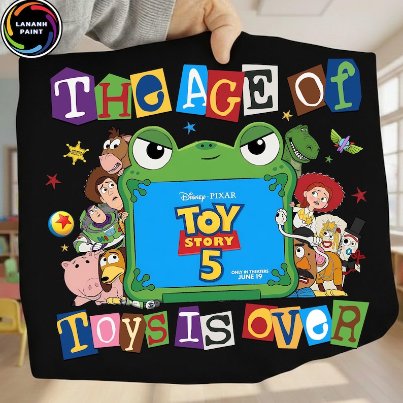 Puede incluir: Un art&iacute;culo de tela negra con un marco central en forma de rana verde que contiene el texto Disney Pixar Toy Story 5 Only in Theaters June 19. Alrededor del marco hay varios personajes animados y el texto The Age of Toys is Over en letras coloridas.