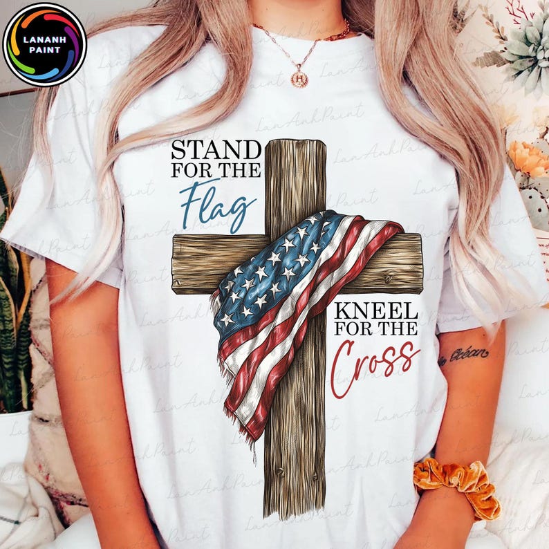 Puede incluir: Camiseta blanca con un dise&ntilde;o de una cruz de madera con una bandera estadounidense. El texto dice "Stand for the Flag" y "Kneel for the Cross". La camiseta tiene cuello redondo.
