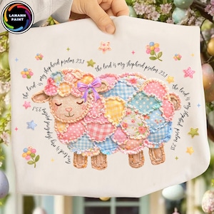 May include: A white fabric item featuring a colorful patchwork sheep design. The sheep has a pink bow and is surrounded by floral and star accents. Text reads "the lord is my shepherd psalm 23:1".