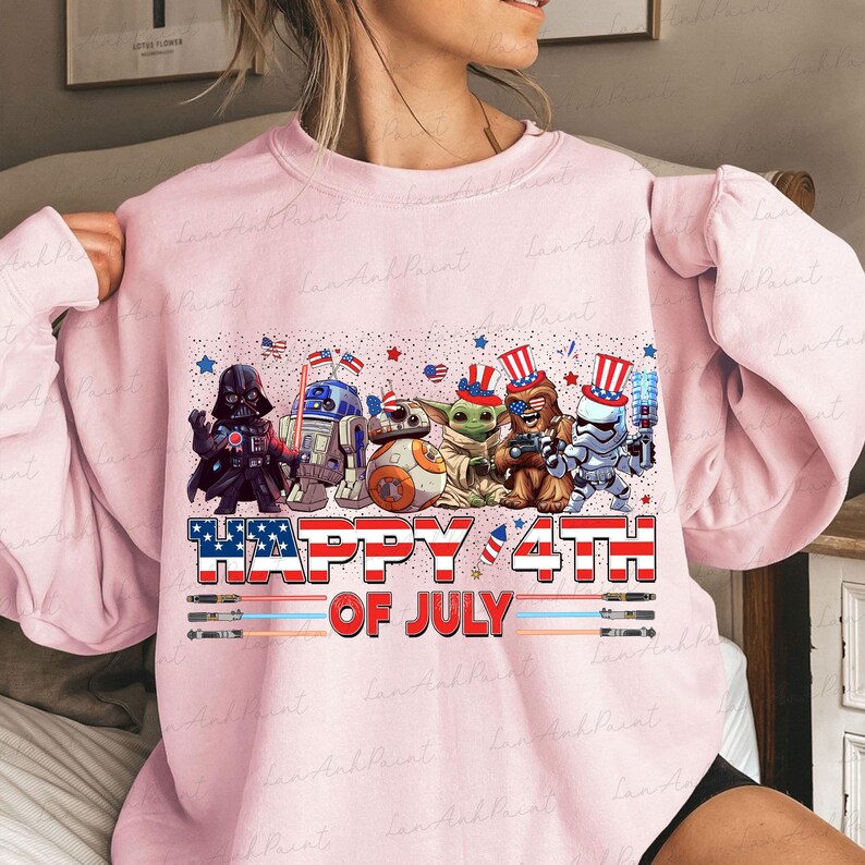 K&ouml;nnte beinhalten: Hellrosa Sweatshirt mit einer Grafik von Star Wars-Charakteren in patriotischer Kleidung, darunter Darth Vader und R2-D2, mit dem Text "Happy 4th of July" in Rot, Wei&szlig; und Blau.
