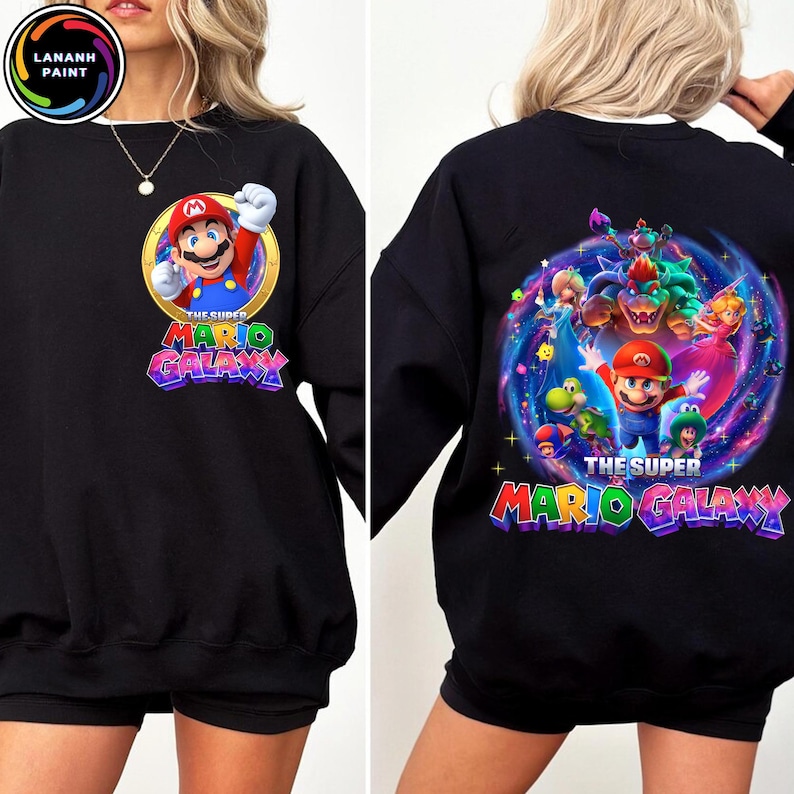 Puede incluir: Sudadera negra con Mario de Super Mario Galaxy. El dise&ntilde;o frontal muestra a Mario en un c&iacute;rculo dorado con el texto "The Super Mario Galaxy". El dise&ntilde;o trasero muestra a Mario y otros personajes en un dise&ntilde;o de galaxia colorido con el mismo texto.