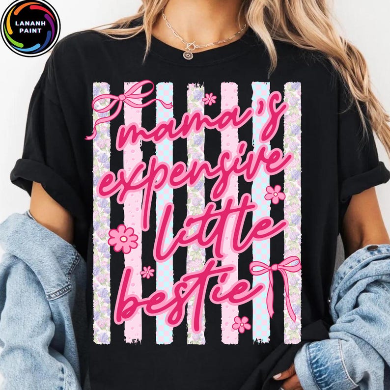 Puede incluir: Camiseta negra con la frase "Mama's Expensive Little Bestie" en rosa. El dise&ntilde;o incluye lazos rosas, flores y rayas verticales en rosa, blanco y azul claro.