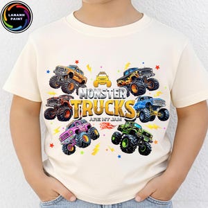 K&ouml;nnte beinhalten: Cremefarbenes T-Shirt mit einem farbenfrohen Monster-Truck-Motiv. Das Design zeigt verschiedene Monster Trucks in Orange, Blau, Gr&uuml;n, Pink und Braun, mit dem Text "Monster Trucks Are My Jam".