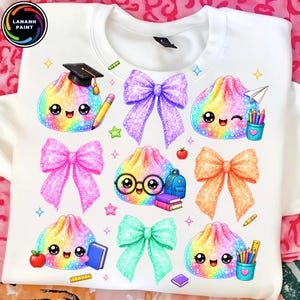 May include: A white sweatshirt featuring a colorful graphic print of multiple rainbow-colored, smiling dumpling characters. The design includes glittery bows in purple, pink, and orange, along with school supplies like pencils, books, and a backpack.