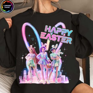 May include: Black sweatshirt with a colorful graphic featuring three stylized figures in Easter bunny ears, the words "HAPPY EASTER", and a cityscape. The design includes pastel colors and a heart.