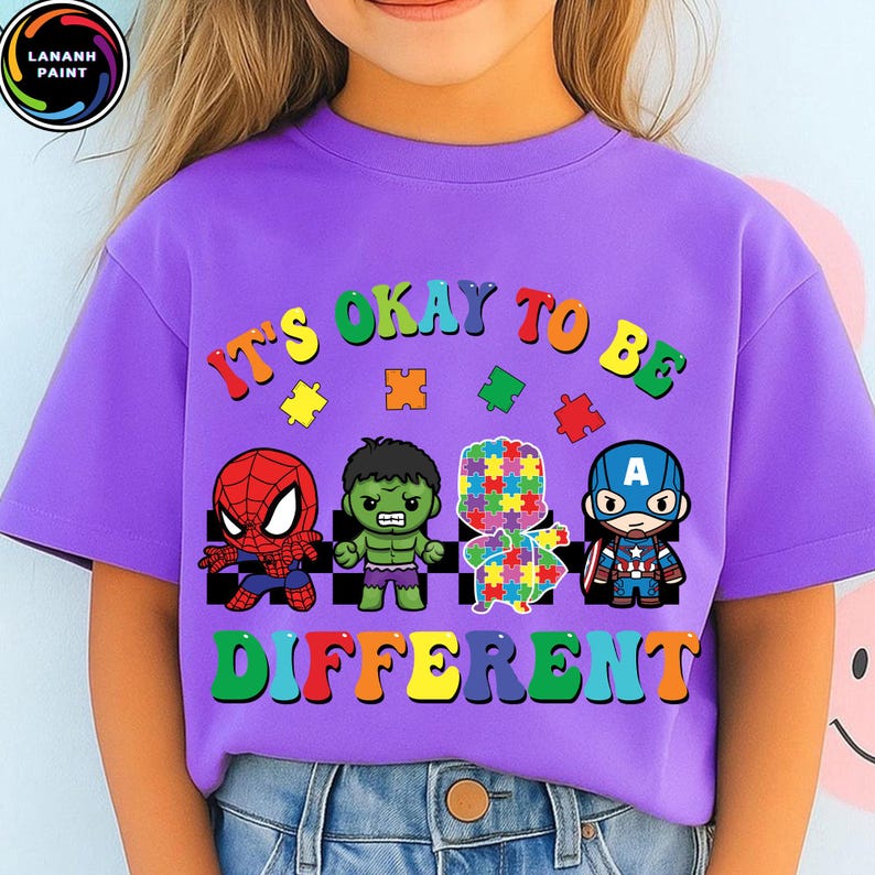 May include: A purple t-shirt with the text "IT'S OKAY TO BE DIFFERENT" in colorful letters. The shirt features cartoon images of Spider-Man, Hulk, a puzzle piece figure, and Captain America.