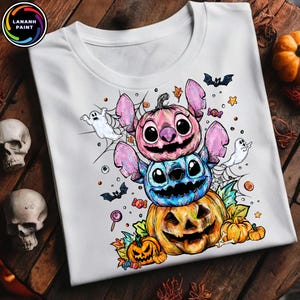 May include: White t-shirt featuring a Halloween-themed design. The design includes a stack of cartoon characters resembling Stitch, each with a pumpkin-like appearance. Bats, ghosts, and candy are also included in the design.