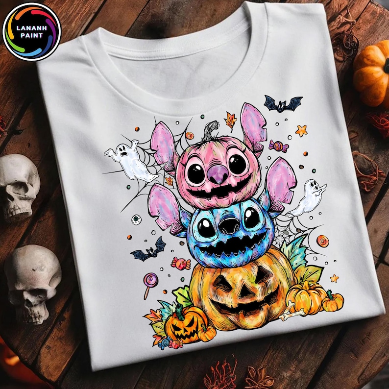May include: White t-shirt featuring a Halloween-themed design. The design includes a stack of cartoon characters resembling Stitch, each with a pumpkin-like appearance. Bats, ghosts, and candy are also included in the design.