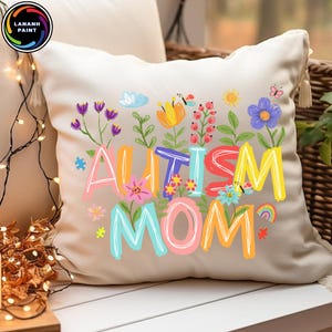 以下が含まれることがあります： カラフルな文字で「AUTISM MOM」と書かれたベージュ色のクッション。花や蝶のイラストで囲まれています。白い表面に置かれています。