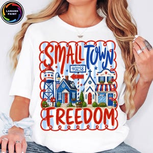 May include: White t-shirt with a patriotic design featuring the words "SMALL TOWN FREEDOM" in red and blue. The graphic includes illustrations of a water tower, houses, and a church, with the zip code 40258.