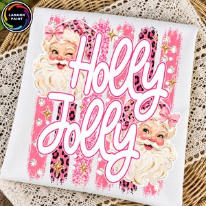 May include: A white t-shirt featuring a graphic print of two vintage-style Santa Claus faces with pink leopard print hats and bows. The text "Holly Jolly" is written in large white script across the center, layered over pink brush strokes.