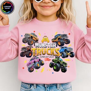 K&ouml;nnte beinhalten: Rosa Sweatshirt mit einem farbenfrohen Monster-Truck-Motiv. Das Design zeigt verschiedene Monster-Truck-Illustrationen, Sterne, Blitze und den Text "MONSTER TRUCKS ARE MY JAM."