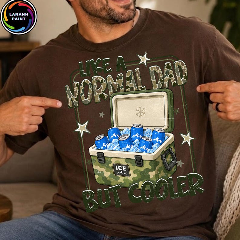 K&ouml;nnte beinhalten: Braunes T-Shirt mit einer Camouflage-K&uuml;hltasche, gef&uuml;llt mit Eis und blauen Dosen. Der Text lautet "LIKE A NORMAL DAD BUT COOLER" in Gr&uuml;n und Wei&szlig;. Das Shirt hat einen Rundhalsausschnitt.