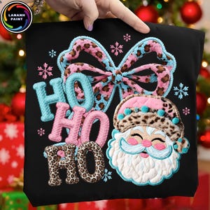May include: Black Christmas-themed tote bag with a festive design. Features the words "HO HO HO" in various colors and patterns, including leopard print. Includes a Santa Claus face and a bow with leopard print accents.