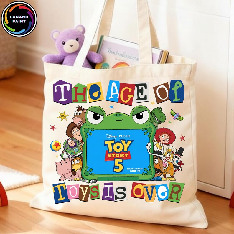 Puede incluir: Un bolso de tela color crema con un estampado gr&aacute;fico colorido de personajes de Toy Story rodeando un marco verde con forma de rana. El texto dice THE AGE OF TOY STORY 5 TOYS IS OVER, junto al logotipo de Disney Pixar y 19 de junio.