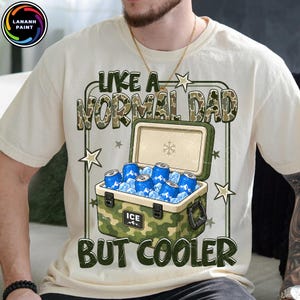 K&ouml;nnte beinhalten: Cremefarbenes T-Shirt mit dem Text "LIKE A NORMAL DAD BUT COOLER" &uuml;ber einer K&uuml;hlbox, die mit blauen Dosen und Eis gef&uuml;llt ist. Die K&uuml;hlbox hat ein Tarnmuster. Das Shirt hat einen Rundhalsausschnitt und kurze &Auml;rmel.