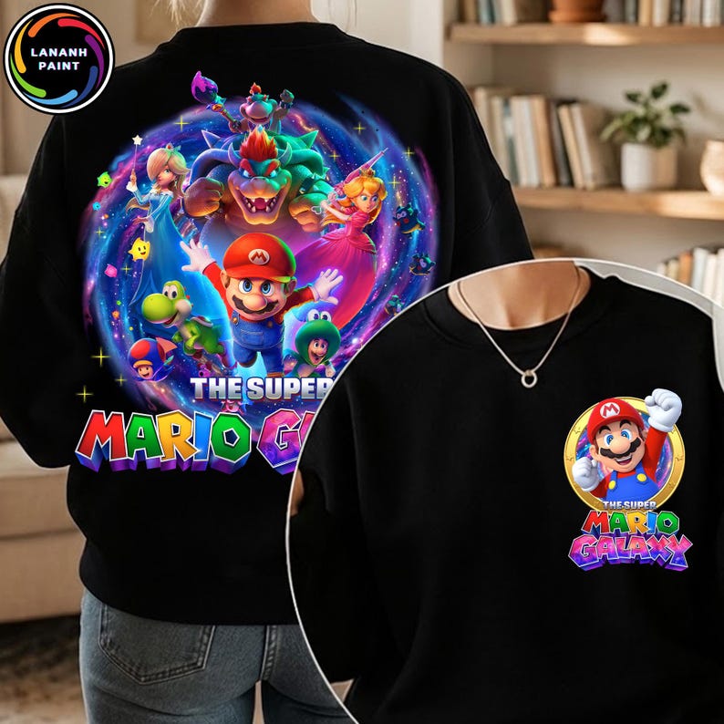 Puede incluir: Sudadera negra con un gr&aacute;fico colorido de Mario y otros personajes del juego Super Mario Galaxy. El dise&ntilde;o incluye el texto "THE SUPER MARIO GALAXY" en una fuente vibrante. Una versi&oacute;n m&aacute;s peque&ntilde;a del dise&ntilde;o est&aacute; en la parte delantera.