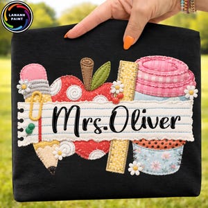 May include: Black tote bag featuring a colorful applique design with school-themed elements. The design includes an apple, pencil, ruler, and cupcake, with the text "Mrs. Oliver" on a lined paper banner. White daisy accents.