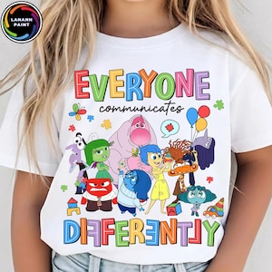 以下が含まれることがあります： 「EVERYONE communicates DIFFERENTLY」の文字と漫画のキャラクターが描かれた白いTシャツ。映画「インサイド・ヘッド」のキャラクターが、さまざまな色と形でデザインされています。
