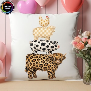 Op de afbeelding: Wit sierkussen met een stapel boerderijdieren: een kip, een schaap, een varken en een koe. De koe heeft een luipaardprint. Het kussen ligt op een houten oppervlak met roze ballonnen en bloemen op de achtergrond.
