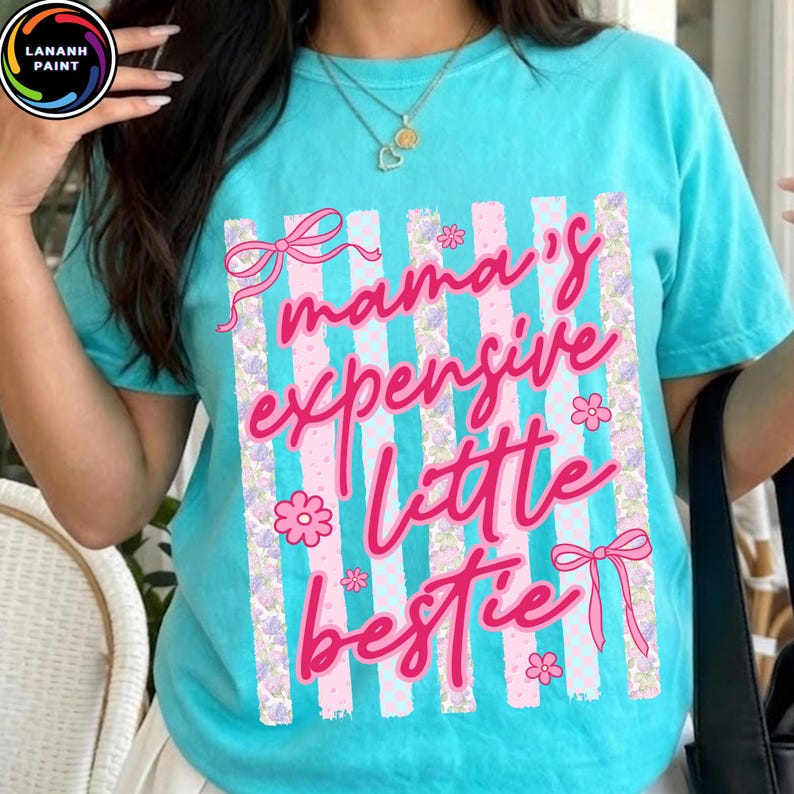 Puede incluir: Camiseta turquesa con la frase rosa "mama's expensive little bestie". El dise&ntilde;o incluye rayas verticales con detalles florales y lazos. La camiseta tiene cuello redondo y mangas cortas.