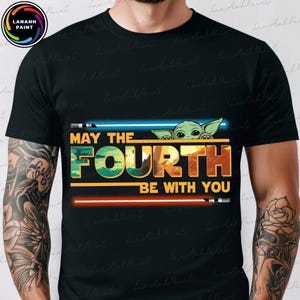 以下が含まれることがあります： 「May the Fourth Be With You」というテキストの上に、緑色のエイリアンのキャラクターがのぞいている黒いTシャツです。