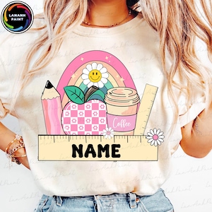 Könnte beinhalten: Ein weißes T-Shirt mit einem rosa, gelben und grünen Regenbogen, einem roten Apfel mit einem weißen und rosa karierten Muster, einer braunen Kaffeetasse mit dem Wort "Coffee" darauf, einem Bleistift und einem Lineal. Der Text "NAME" befindet sich auf einem gelben Rechteck.