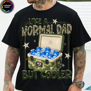 K&ouml;nnte beinhalten: Schwarzes T-Shirt mit dem Text "LIKE A NORMAL DAD BUT COOLER" in Gr&uuml;n und Camouflage-Print. Die Grafik zeigt eine K&uuml;hlbox mit blauen Dosen und Eis, mit Sternakzenten.