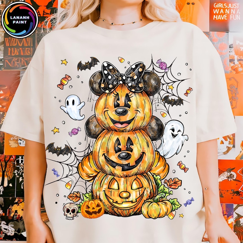 May include: Cream-colored t-shirt featuring a stacked pumpkin design resembling Minnie Mouse, complete with a bow, ears, and a smiling jack-o'-lantern face. Halloween-themed with ghosts, bats, and candy.