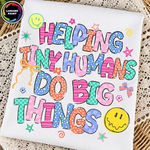 Op de afbeelding: Een wit t-shirt met de kleurrijke tekst HELPING TINY HUMANS DO BIG THINGS in diverse patronen zoals strepen, ruitjes en bloemen. Het ontwerp is versierd met gele smileys, kleine sterretjes, bloemetjes en strikjes.