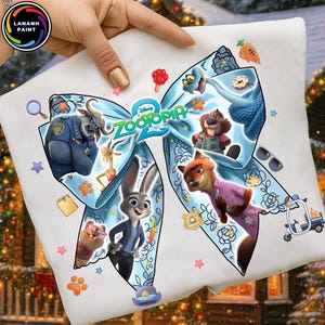 May include: White t-shirt featuring a large, light blue bow design with characters from the Disney movie "Zootopia 2". The bow is decorated with floral patterns and various cartoon images, including a police officer and a rabbit.
