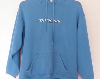 Può includere: Una felpa con cappuccio blu chiaro con un logo ricamato bianco che dice "Billabong since 1973".