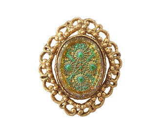 May include: Vintage gold-toned brooch with an oval, iridescent center featuring a green starburst pattern. The brooch has a decorative, openwork frame with floral and beaded details, creating a classic, ornate design.