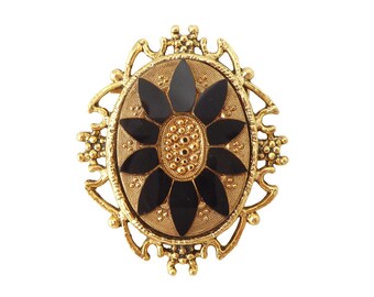 May include: A vintage gold-tone brooch with an oval shape. The center features a black flower design with a textured gold center. The brooch is framed by an ornate gold border with decorative elements, creating a classic, elegant look.