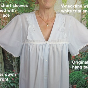 May include: A light blue nightgown with a V-neckline, white lace trim, and wide short sleeves. The nightgown has a button-up front and a delicate floral pattern on the neckline. The image includes the text "Original paper hang tag".