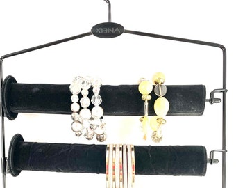 May include: Black metal jewelry hanger with six velvet-covered rods for storing bracelets. The hanger has a hook at the top and the brand name "XENA" is printed on the top bar.