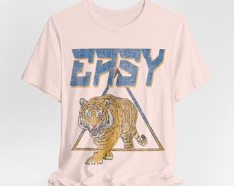 May include: A pink t-shirt with a vintage-style graphic of a tiger in a triangle with the word "EASY" above it.