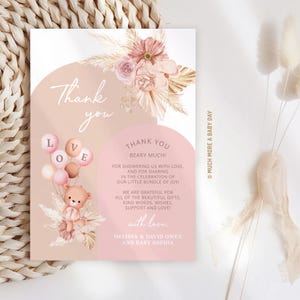 May include: Thank you card with a pink and brown color scheme. The card features a teddy bear holding balloons that say "LOVE" and a floral arrangement. The text on the card reads "Thank you beary much!" and includes a message of gratitude for gifts and support. The card is signed "Melissa & David Owen and Baby Sophia".