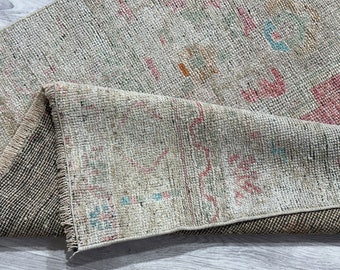 May include: A close-up of a beige rug with a faded, multi-colored pattern. The rug has a fringe border and is folded in half.