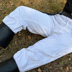 Puede incluir: Pantal&oacute;n blanco de lino con cintur&oacute;n de cuero negro y bolsa de cuero negro. El pantal&oacute;n es holgado y tiene cintura con cord&oacute;n.