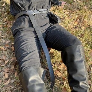 Puede incluir: Una persona que lleva pantalones negros con un cintur&oacute;n de cuero negro y una bolsa de cuero negra. La persona lleva botas negras de ca&ntilde;a alta.